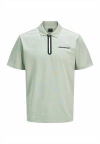Lys grøn kortærmet polo shirt med en sort lynlås ved kraven og et lille sort logo på brystet. Glat stoftekstur.