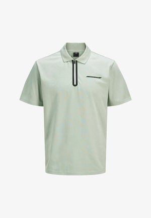 Világos zöld, rövid ujjú pólóing, fekete cipzárral a gallérnál és egy kis fekete logóval a mellrészen. Simább anyagtextúra.