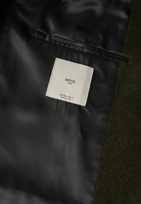 Zwart stoffen interieur met een in crèmekleur gestikt label, waarop "MNG" en zorginstructies staan. Soepele textuur, schone randen en een minimalistisch ontwerp.