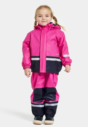 Veste imperméable rose avec des poignets élastiques, assortie à un pantalon rose et marine. Les bandes réfléchissantes améliorent la visibilité.