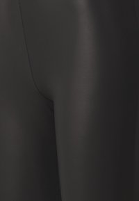 Leggings noirs avec une texture lisse et brillante. Ils présentent un design ajusté et des coutures minimales, mettant en valeur un aspect épuré.
