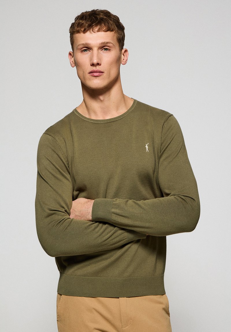 Suéter de punto verde oliva con mangas largas, diseño de cuello redondo y puños acanalados. Presenta un pequeño logo bordado en el pecho.
