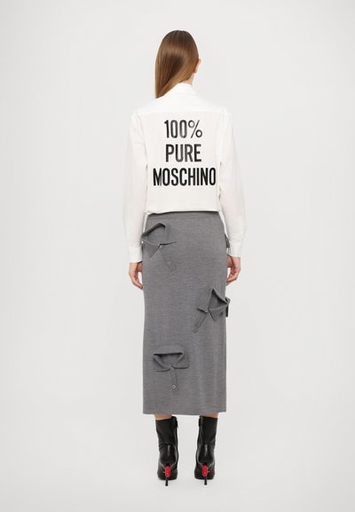 Cămașă albă cu textul "100% PURE MOSCHINO" în font mare, negru, asortată cu o fustă gri cu detalii de guler supradimensionat și cizme negre până la gleznă.