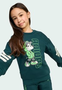 Green sweatshirt featuring a cartoon character with headphones and text. It has white stripes on the sleeves and a relaxed fit design.