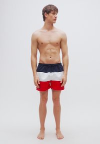 Μαγιό βερμούδα με μπλοκ χρωμάτων σε ναυτικό μπλε, λευκό και κόκκινο. Κατασκευασμένο από ελαφρύ υλικό με ελαστική μέση και κορδόνι, σχεδιασμένο να φτάνει μέχρι το γόνατο.