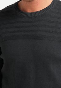 Schwarzer Strickpullover mit einem strukturierten horizontalen Streifendesign an der Brust. Verfügt über einen gerippten Rundhalsausschnitt und eine glatte Oberflächenstruktur.