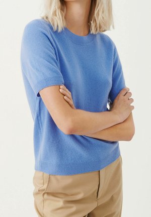 Jasnoniebieski sweter z krótkim rękawem i okrągłym dekoltem, wykonany z miękkiego materiału, z prążkowanymi krawędziami przy rękawach i u dołu.