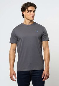 Harmaa lyhythihainen t-paita, joka on valmistettu pehmeästä puuvillasekoitteesta. Paidan kauluksessa on pyöreä pääntie, ja vasemmassa rinnassa on pieni sininen logo.