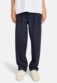 Navy blue wide-leg trousers made of cotton, featuring a relaxed fit, with side pockets and a smooth texture. Worn with white sneakers.