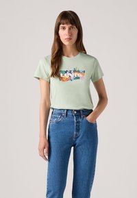 Lysegrønn bomullst-skjorte med et fargerikt blomsterdesign og teksten "Levi’s". Kombinert med høyt liv blå denimjeans.