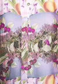 Mehrfarbiges Hemd mit lebendigen Früchte- und Pflanzenmustern in Grüntönen, Lila und Pink. Glatter, strukturierter Stoff mit Knopfdetails.