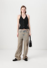 Svart halterneck crop vest med knappdetaljer, kombinert med løse beige jeans. Svart håndveske og svarte sko fullfører antrekket. Minimalistisk design, glatt tekstur.