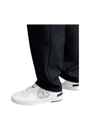 Baskets blanches avec une tige texturée, détail de logo sur le côté et accents noirs, accompagnées d'un pantalon noir ample.