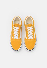 Gule semskede sneakers med hvite snøringer og sidestriper, med avrundet tå og svart gummisåle. Stilige sømdetaljer over hele designet.