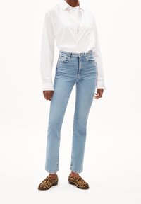 Light blue high-waisted jeans with a slim fit, paired with a white button-up shirt and leopard print loafers.