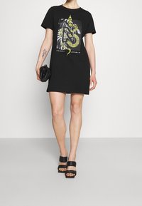 Czarna sukienka t-shirt z krótkim rękawem z kolorowym motywem węża na froncie. Stylizowana z małą czarną torebką i czarnymi sandałami na obcasie.
