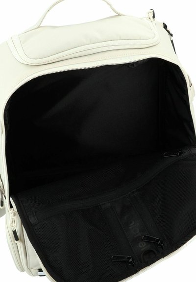 Mochila de color crema con una parte superior con cremallera, interior negro y bolsillo de malla. Presenta una tela duradera y cremalleras resistentes.