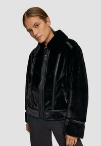 Schwarze Kunstfelljacke mit Zipper vorne, breitem Kragen und Seitentaschen, versehen mit glatten Lederakzenten und einer flauschigen Textur.