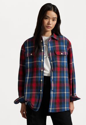 Plaid flannel shirt in red, blue, and black. Button-down design with two chest pockets and rolled sleeves, featuring a textured fabric.