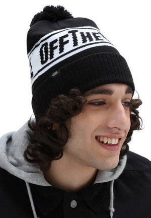 Gorro de punto en blanco y negro con un pompón en la parte superior, que presenta un patrón de texto audaz y una pequeña etiqueta de logotipo, textura acanalada y un ajuste ceñido.