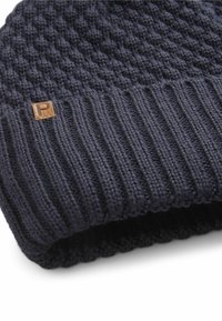 Knitted dark navy beanie with a textured pattern and a wide ribbed cuff; features a small rectangular logo patch in brown.