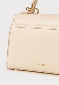 Bolso de mano de cuero beige con herrajes dorados, un diseño estructurado y costuras visibles. Cuenta con una correa de hombro desmontable y detalle del logo.