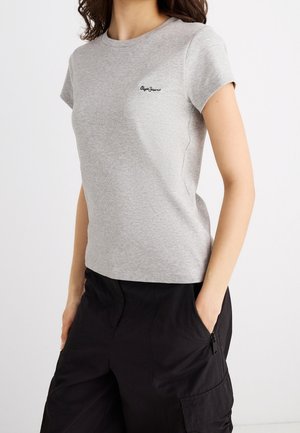 Kobieta ubrana w dopasowaną, jasnoszarą koszulkę z krótkim rękawem z logo „Pepe Jeans” oraz czarne spodnie typu cargo z kieszeniami na suwak.
