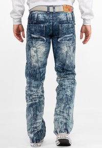 Jeans in denim blu sbiaditi con una finitura testurizzata, dotati di molteplici tasche e una cintura grigia, visti da dietro.