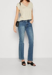 Beige V-hals T-shirt med tekstureret kant, parret med mørkeblå flared jeans. Sorte open-toe blockhæle sandaler og en lille sort håndtaske.