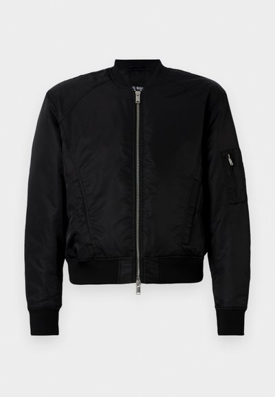 Casaco bomber preto feito em tecido suave, com fecho frontal em zíper, punhos canelados e um bolso com zíper na manga esquerda.