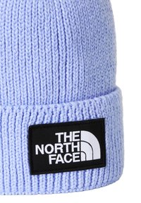 Gorro tejido azul claro con textura acanalada y puño doblado, con un parche de logo rectangular negro con texto y gráfico blancos.