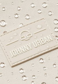 Fehér szövet vízcseppekkel és egy megemelt, krém színű betűkkel ellátott, "JOHNNY URBAN" feliratú, texturált folttal.