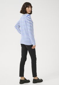 Haut à manches longues rayé bleu et blanc avec un col rond, associé à un pantalon noir ajusté et des chaussures noires, vu de dos.