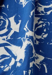 Tissu bleu et blanc avec des motifs floraux abstraits style coups de pinceau ressemblant à des roses sur une surface textile légèrement froissée.
