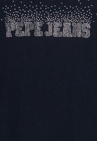 Tmavá tkanina s nápisem "PEPE JEANS" vyloženým rozptýlenými stříbrnými kamínky ve středu nahoře.