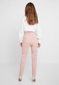 Pantalons taille haute rose clair à coupe slim, fabriqués dans un tissu lisse, avec des poches arrière et des passants de ceinture.