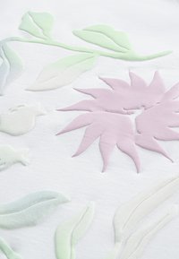 Υφασμα με υφή που παρουσιάζει ανάγλυφα λουλουδένια μοτίβα σε απαλούς παστέλ τόνους: ανοιχτοπράσινα φύλλα και ένα ανοιχτό ροζ λουλούδι σε λευκό φόντο.