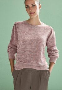 Pulover texturat roz, cu guler și mansete ribate, având umeri ușor bufanți și o croială lejeră, asortat cu pantaloni bej cu talie înaltă.