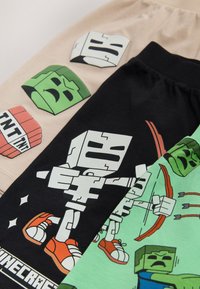 Trois t-shirts présentent des motifs Minecraft : noir avec un personnage, vert avec un archer, et beige avec des visages de blocs ; en coton, couleurs variées.