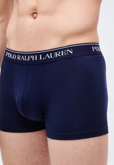 Ανδρικός κορμός που φοράει μπλε ναυτικό boxer briefs Polo Ralph Lauren με λογότυπο στη μέση, εμφανίζοντας το κάτω μέρος της κοιλιάς και το πάνω μέρος των μηρών.