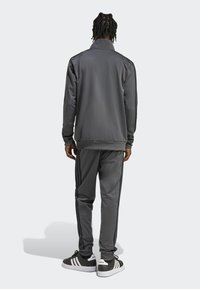 Conjunto de chándal gris que incluye una chaqueta con cremallera y pantalones, ambos de tela suave con rayas laterales negras, combinado con zapatillas negras y blancas.
