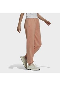 Persikofärgade mjukisbyxor i mjukt tyg med sidofickor och avslappnad passform, i kombination med ljusa sportskor med texturerade sulor.