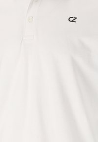 Vit polo skjorta i bomull med en texturerad yta, med en svart logotyp på vänster bröst och två knappstängning.