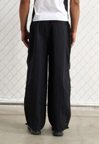 Svarta vida byxor i lätt strukturerad tyg, med sidofickor och elastiska manschetter vid anklarna.