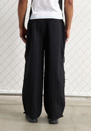 Svarta vida byxor i lätt strukturerad tyg, med sidofickor och elastiska manschetter vid anklarna.