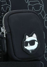 Schwarze Stoff-Täschchen mit Reißverschluss, das ein weißes Katzenemblem mit Sonnenbrille zeigt. Die Oberfläche hat ein leicht strukturiertes Finish mit kontrastierenden Umrissen.