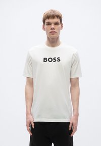 Valge lühikeste varrukatega puuvillast t-särk, millel on esiküljel silmapaistev must "BOSS" logo; sile tekstuur, ümar kaelus.