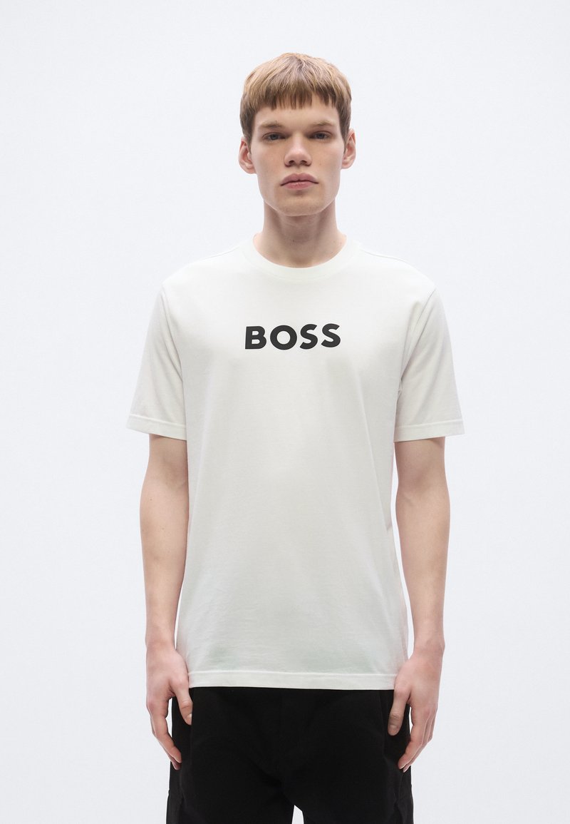 Valge lühikeste varrukatega puuvillast t-särk, millel on esiküljel silmapaistev must "BOSS" logo; sile tekstuur, ümar kaelus.