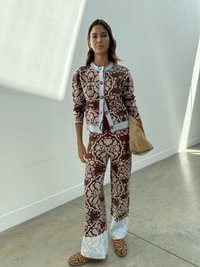 Brauner gemusterter Cardigan mit hellblauen Akzenten, passende braune Hose mit blauen Säumen und Leopardenmuster-Schuhe. Hält eine sandfarbene Tasche.