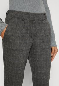 Grijze geruite broek met een getailleerde pasvorm, met een zachte textuur en zijzakken, gecombineerd met een geribbelde grijze trui.